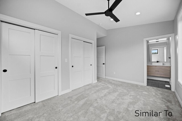 unfurnished bedroom featuring ensuite bath, multiple closets, light colored carpet, lofted ceiling, and ceiling fan