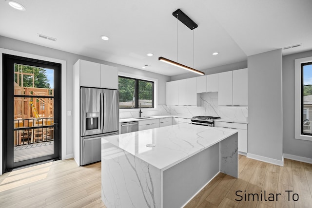 kitchen featuring pendant lighting, white cabinetry, a center island, appliances with stainless steel finishes, and light hardwood / wood-style floors