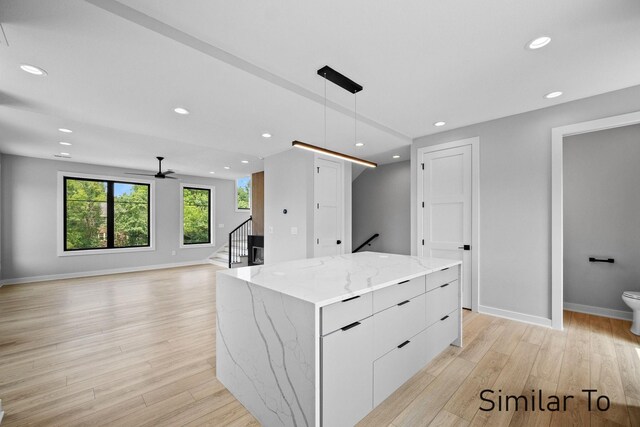 kitchen with pendant lighting, a kitchen island, light stone countertops, white cabinets, and light hardwood / wood-style floors