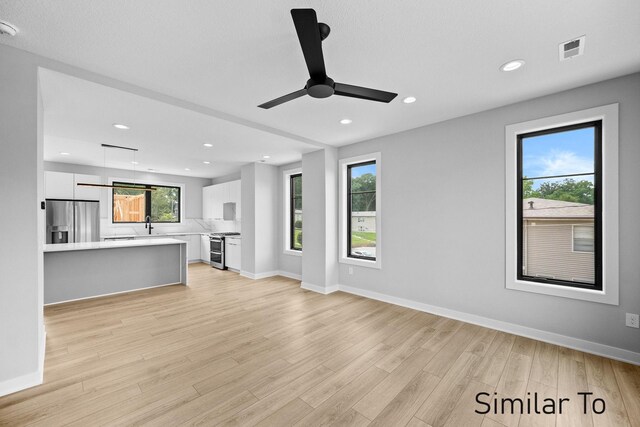 unfurnished living room with a wealth of natural light, ceiling fan, and light wood-type flooring