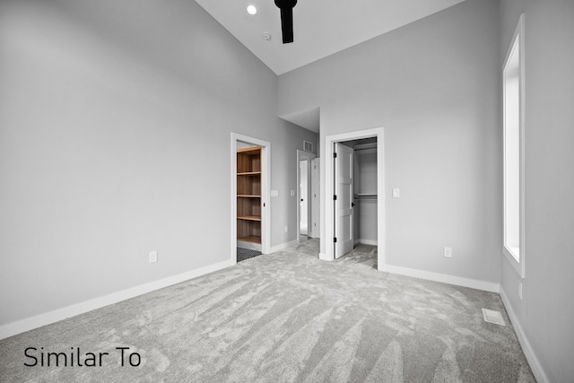 unfurnished bedroom featuring light carpet, ceiling fan, a walk in closet, a closet, and high vaulted ceiling