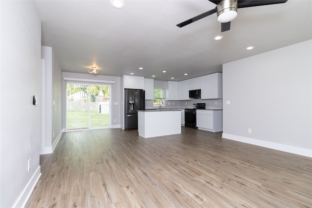 kitchen with light hardwood / wood-style floors, white cabinetry, black appliances, ceiling fan, and a kitchen island