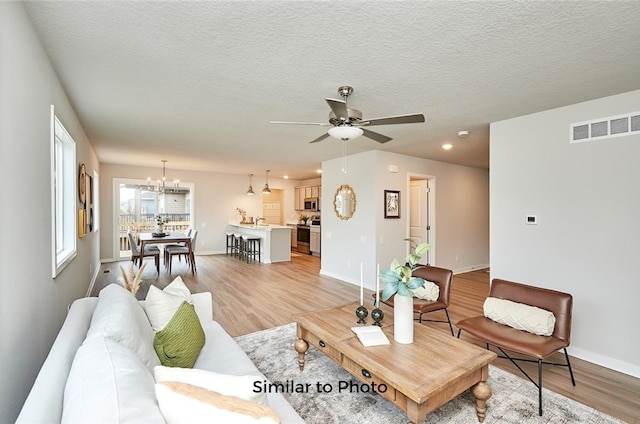 living room with light hardwood / wood-style flooring, ceiling fan with notable chandelier, a textured ceiling, and sink