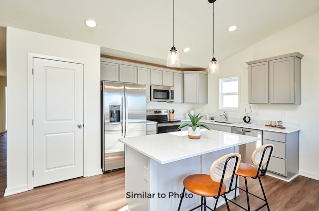 kitchen featuring stainless steel appliances, light hardwood / wood-style flooring, a center island, pendant lighting, and vaulted ceiling