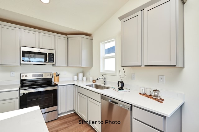 kitchen featuring stainless steel appliances, sink, light hardwood / wood-style flooring, and vaulted ceiling