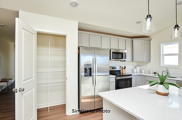 kitchen featuring appliances with stainless steel finishes, hanging light fixtures, light hardwood / wood-style flooring, gray cabinetry, and vaulted ceiling