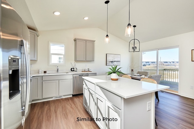 kitchen featuring wood-type flooring, decorative light fixtures, vaulted ceiling, and stainless steel appliances