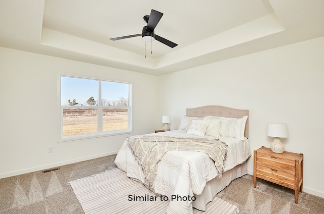 carpeted bedroom featuring ceiling fan and a raised ceiling