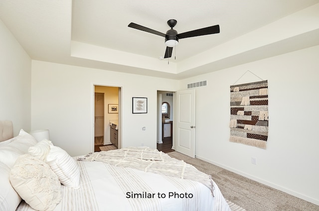 bedroom featuring ensuite bathroom, ceiling fan, a tray ceiling, and carpet