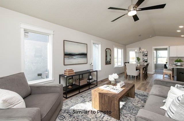 living room featuring light wood-type flooring, ceiling fan with notable chandelier, and vaulted ceiling