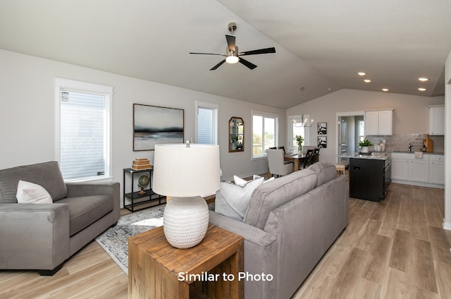 living room with light wood-type flooring, ceiling fan, sink, and vaulted ceiling