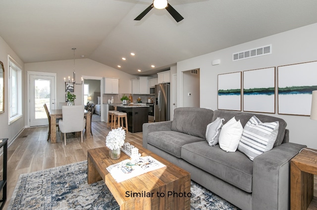 living room with light hardwood / wood-style floors, ceiling fan with notable chandelier, and vaulted ceiling