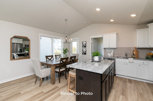 kitchen featuring stainless steel appliances, a center island, vaulted ceiling, white cabinetry, and light hardwood / wood-style flooring