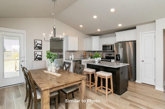 kitchen with white cabinetry, appliances with stainless steel finishes, light stone countertops, a center island, and vaulted ceiling