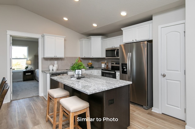 kitchen featuring white cabinetry, appliances with stainless steel finishes, vaulted ceiling, and a center island