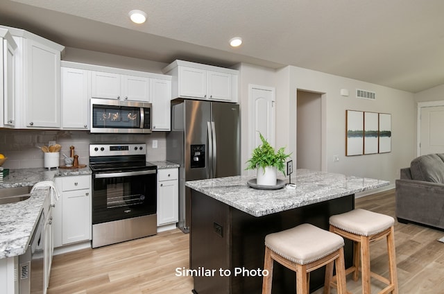 kitchen featuring stainless steel appliances, white cabinetry, light hardwood / wood-style flooring, and a kitchen island