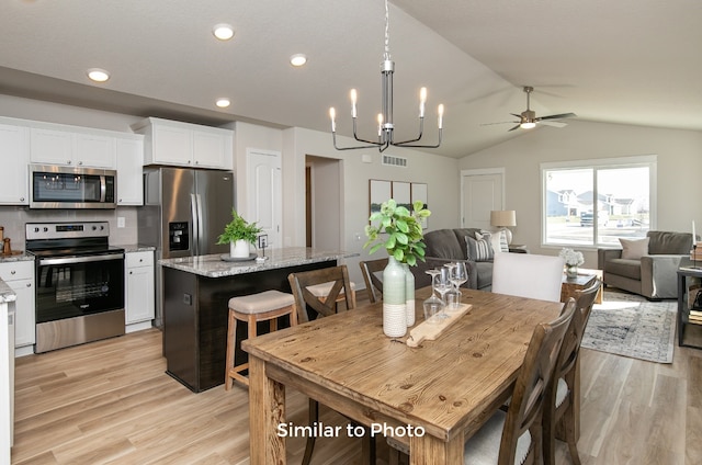 dining area with ceiling fan with notable chandelier, light hardwood / wood-style flooring, and vaulted ceiling