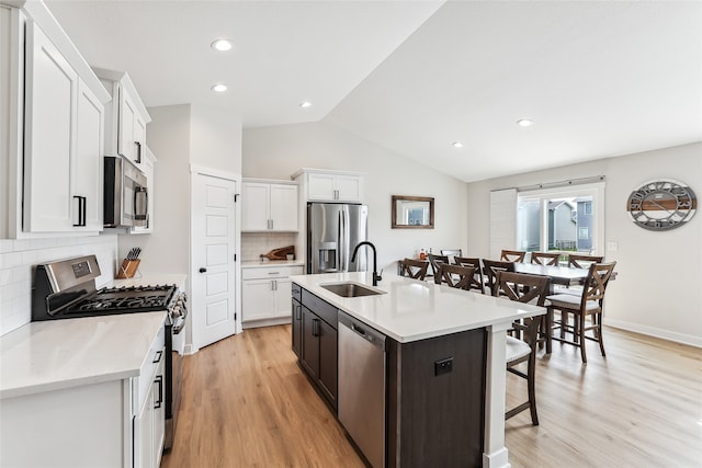 kitchen with tasteful backsplash, stainless steel appliances, a kitchen island with sink, light hardwood / wood-style floors, and lofted ceiling