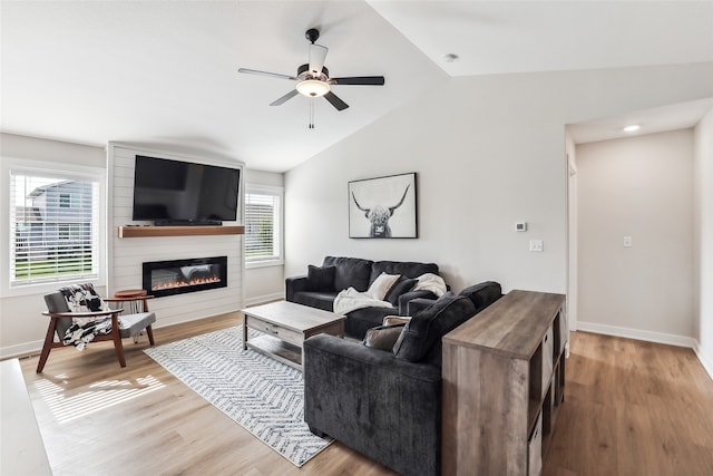 living room featuring ceiling fan, a large fireplace, vaulted ceiling, and light wood-type flooring