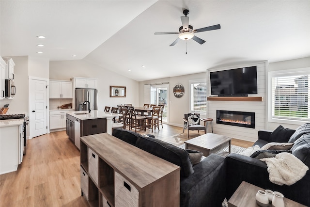 living room with light wood-type flooring, a large fireplace, vaulted ceiling, and a healthy amount of sunlight