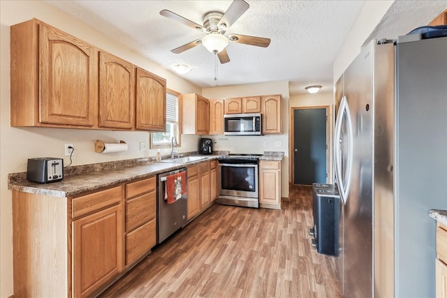 kitchen with appliances with stainless steel finishes, a textured ceiling, ceiling fan, hardwood / wood-style flooring, and sink