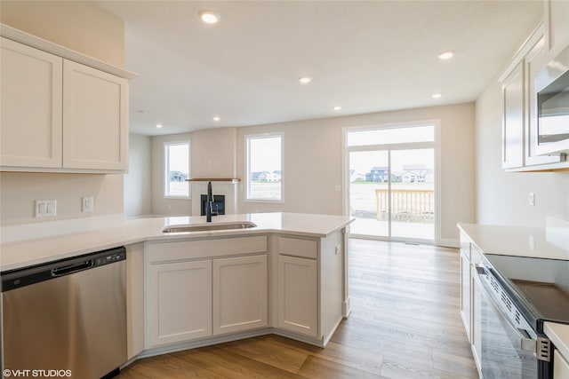 kitchen with kitchen peninsula, appliances with stainless steel finishes, sink, light hardwood / wood-style flooring, and white cabinetry