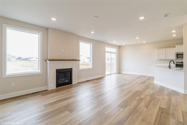 1109 Mulberry Dr NW, Bondurant, IA 50035 - unfurnished living room with recessed lighting, a glass covered fireplace, light wood-style floors, and a sink
