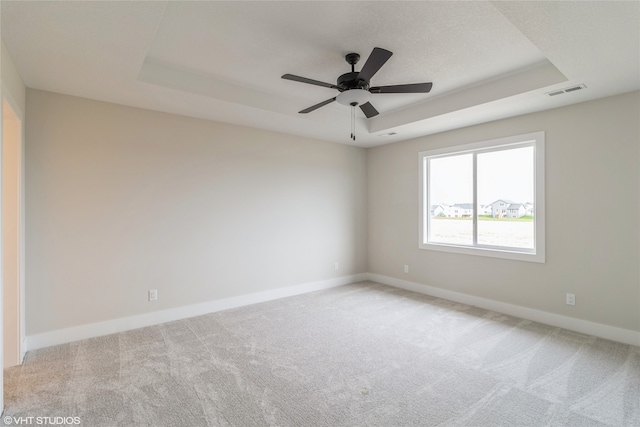 spare room with ceiling fan, a raised ceiling, and light carpet