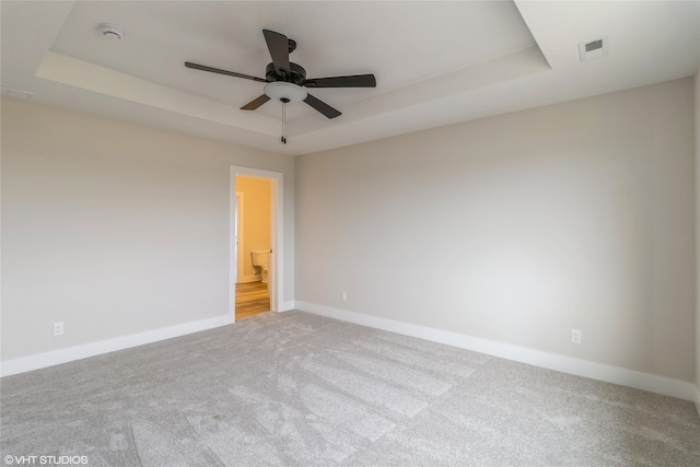 carpeted spare room with a tray ceiling and ceiling fan