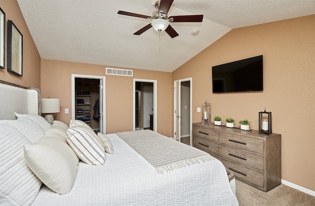 bedroom featuring light colored carpet, lofted ceiling, a walk in closet, a closet, and ceiling fan