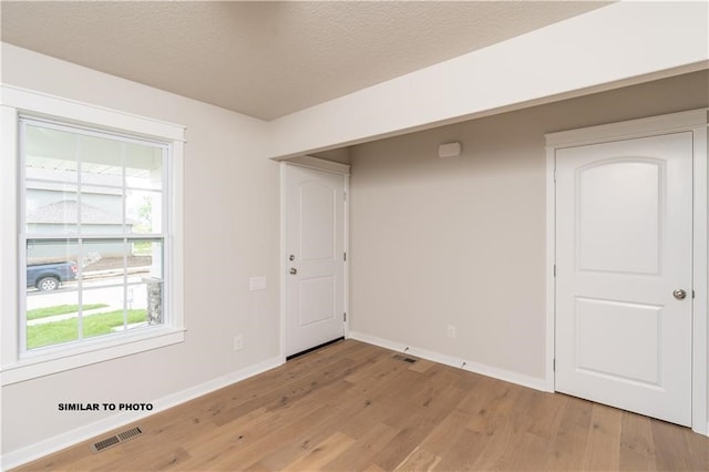 unfurnished room with a textured ceiling and light hardwood / wood-style flooring