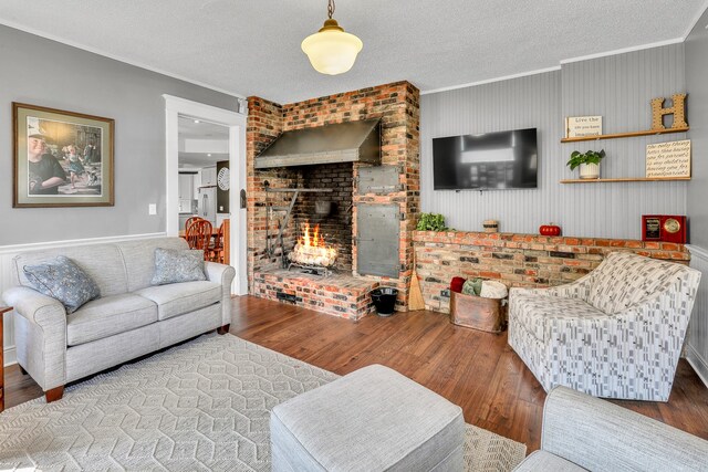 living room with wood-type flooring, ornamental molding, a textured ceiling, and a brick fireplace