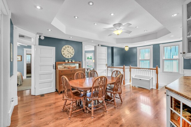 dining room with a raised ceiling, ceiling fan, beverage cooler, and light wood-type flooring