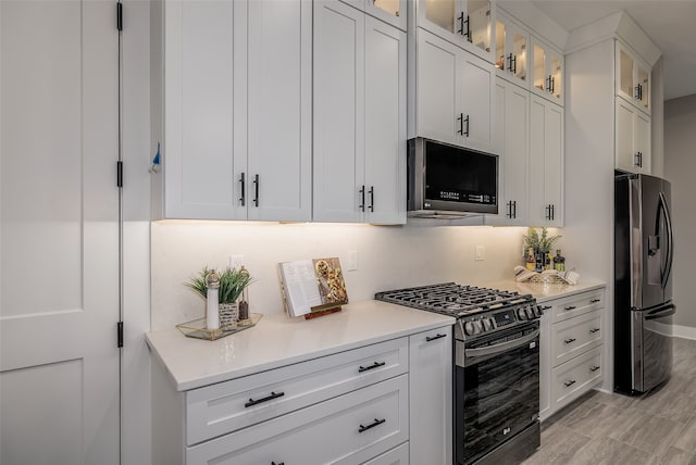 kitchen featuring appliances with stainless steel finishes, white cabinetry, light hardwood / wood-style flooring, and backsplash