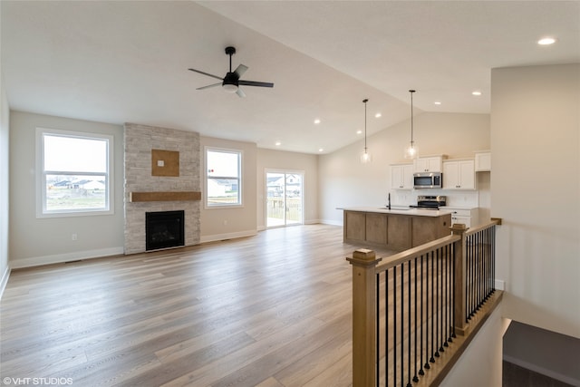 living room featuring plenty of natural light, light hardwood / wood-style floors, a stone fireplace, and vaulted ceiling