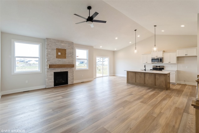 kitchen with white cabinetry, stainless steel appliances, light hardwood / wood-style floors, lofted ceiling, and a center island with sink