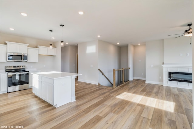 kitchen featuring appliances with stainless steel finishes, light hardwood / wood-style flooring, white cabinets, a kitchen island, and hanging light fixtures