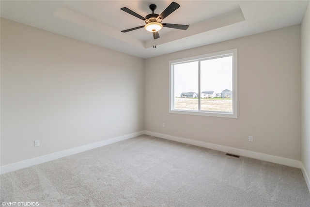 spare room featuring a raised ceiling, ceiling fan, and carpet flooring