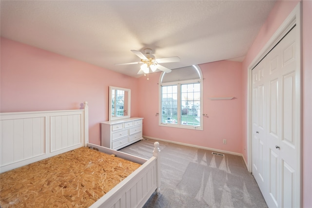 unfurnished bedroom featuring ceiling fan, light colored carpet, a textured ceiling, and a closet