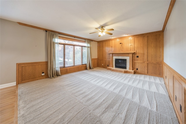 unfurnished living room featuring light carpet, ceiling fan, wooden walls, crown molding, and a tile fireplace