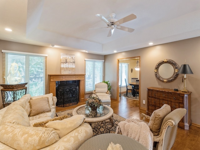 living room featuring a raised ceiling, a fireplace, ceiling fan, and hardwood / wood-style flooring