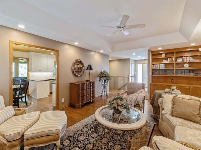 living room featuring ceiling fan, light wood-type flooring, and a raised ceiling