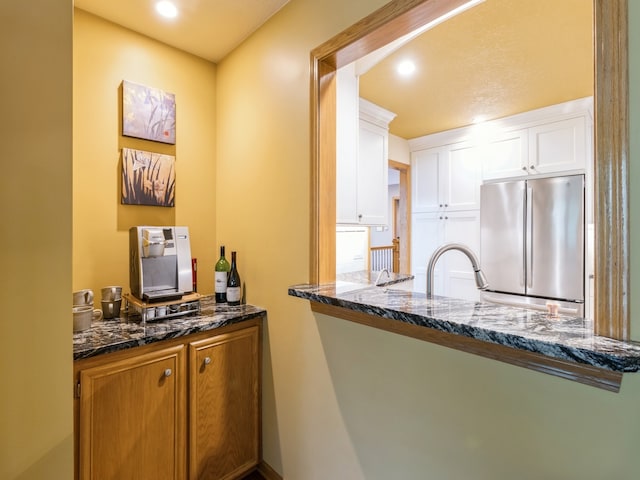 kitchen featuring high end refrigerator, dark stone countertops, sink, and white cabinets