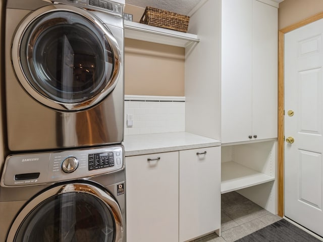 clothes washing area featuring cabinets, light tile patterned floors, a textured ceiling, and stacked washing maching and dryer