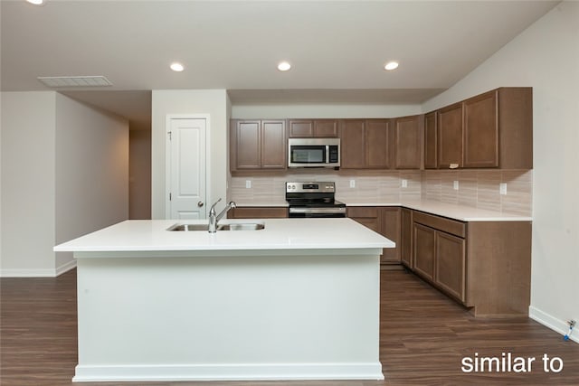 kitchen featuring sink, stainless steel appliances, tasteful backsplash, dark hardwood / wood-style floors, and a center island with sink