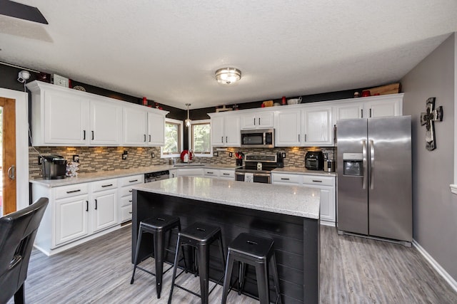 kitchen with hardwood / wood-style flooring, a kitchen island, stainless steel appliances, and white cabinetry