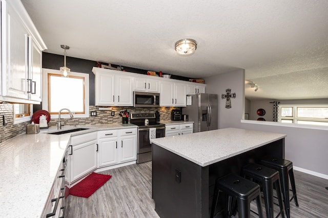 kitchen featuring wood-type flooring, tasteful backsplash, sink, white cabinets, and appliances with stainless steel finishes