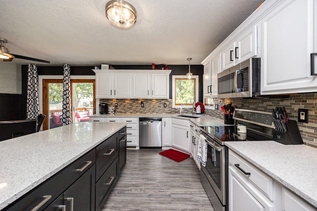 kitchen with pendant lighting, light hardwood / wood-style floors, white cabinetry, decorative backsplash, and appliances with stainless steel finishes