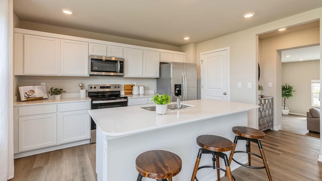 kitchen featuring stainless steel appliances, sink, light hardwood / wood-style floors, white cabinetry, and an island with sink