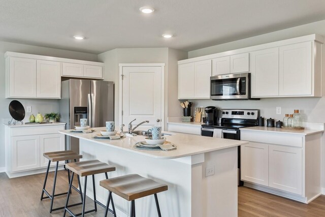 kitchen featuring a center island with sink, white cabinets, light hardwood / wood-style floors, and appliances with stainless steel finishes